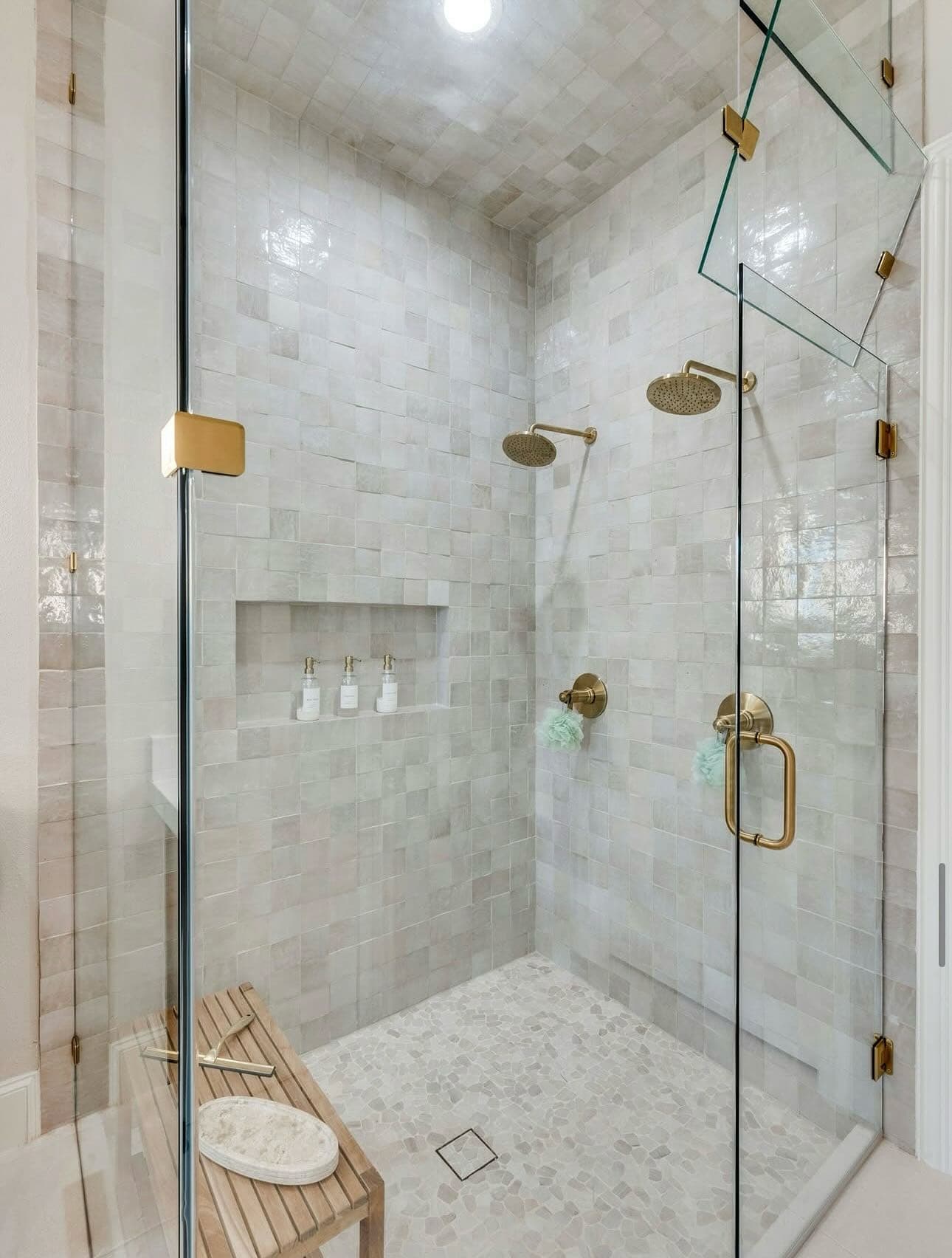 A finished walk-in shower with marble-look tile, a glass enclosure, a built-in niche and two brass rainfall shower heads