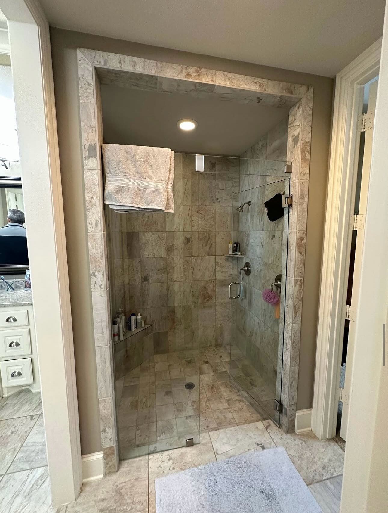 A bathroom with a dated stone-tiled shower enclosure and an older glass door