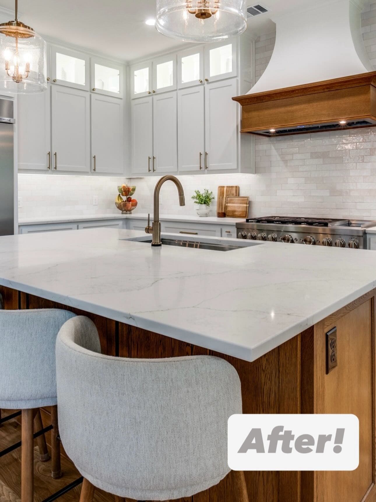 A finished kitchen with white upper cabinets, a stone-topped island with seating, a timber extractor hood and a brass tap